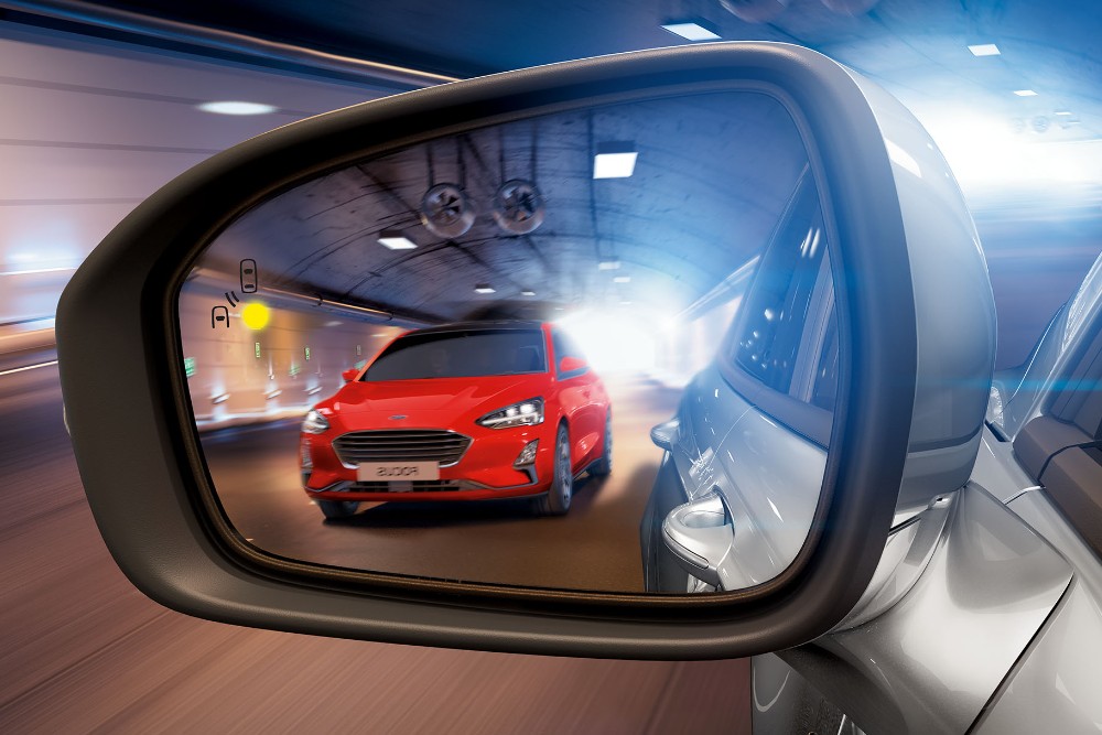 A red Ford Focus is visible in the rearview mirror displaying blind spot information technology.