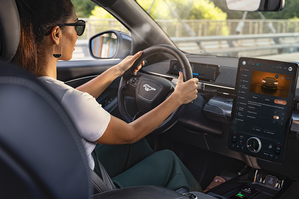 A woman driving the Mustang Mach-E with her hands on the steering wheel. The 15.5" touchscreen shows details about the car.
