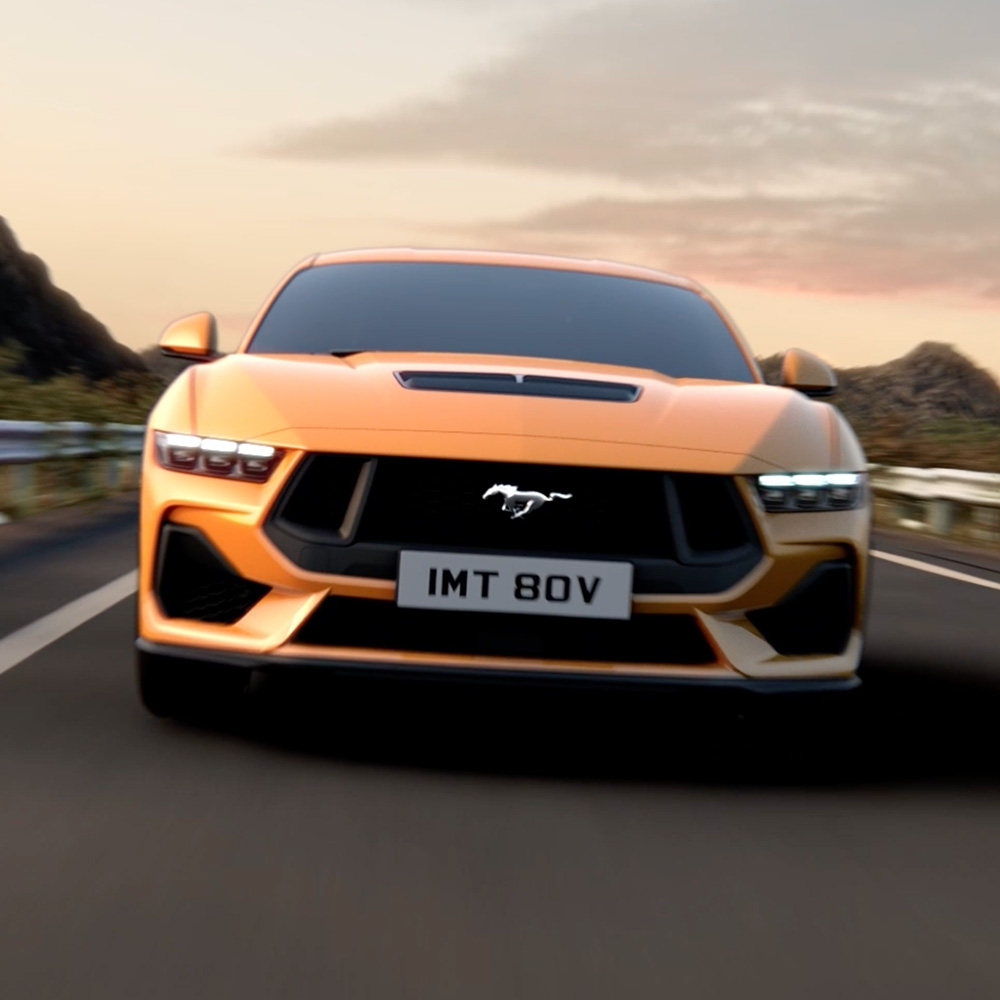 Front view of an orange Ford Mustang with close-up focus on the headlights, grille and Mustang badge.