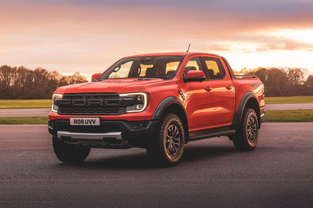 An orange Ford Ranger Raptor pick-up truck parked in a scenic landscape.
