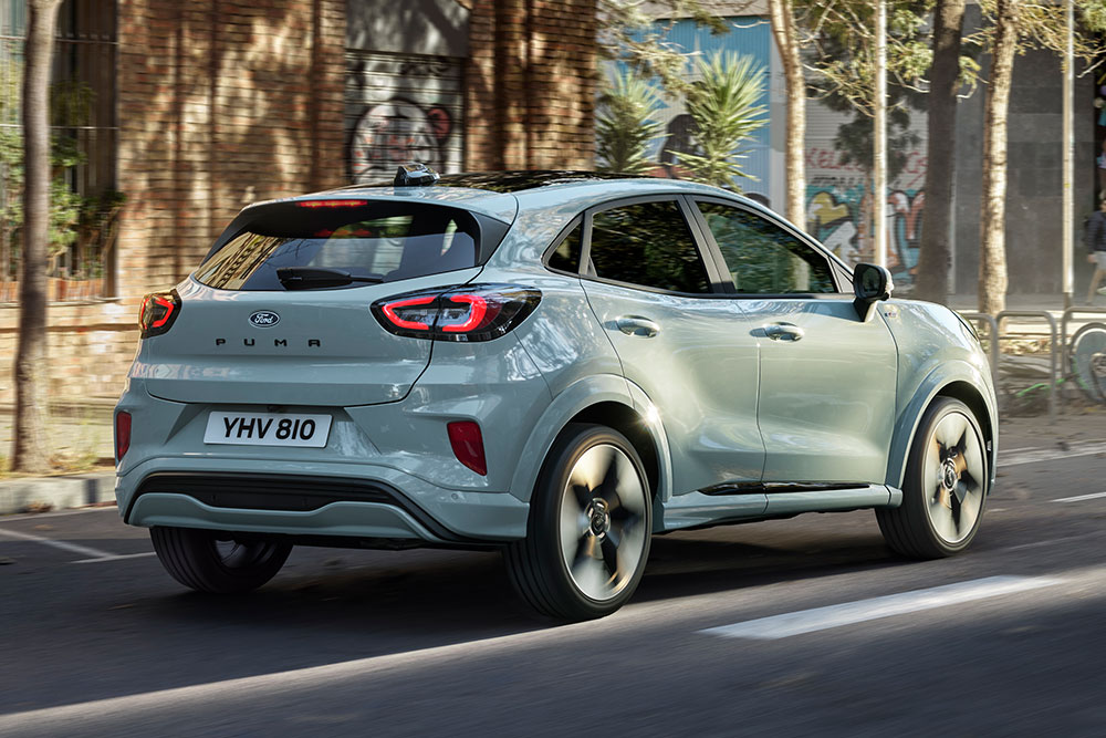 Rear view of a grey Ford Puma driving on a city street with people and buildings. 