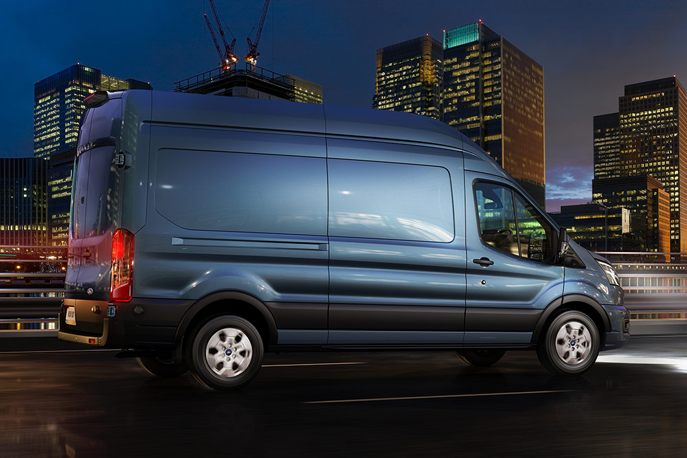 Blue Ford Transit drives on a city street at night.