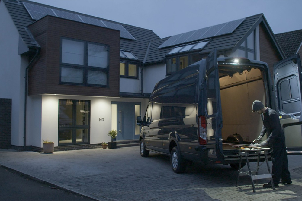 A carpenter works behind a Ford Transit Van with open rear doors at night, illuminated by the LED downlighter.