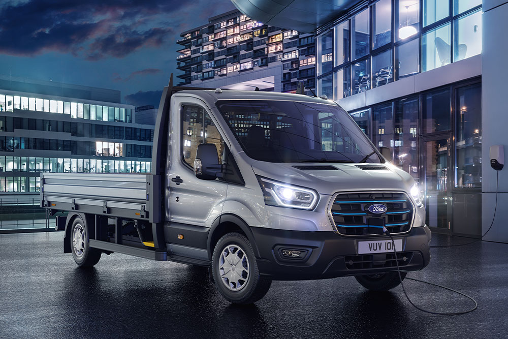 Silver Ford E-Transit Chassis Cab parked in front of a modern building at night.