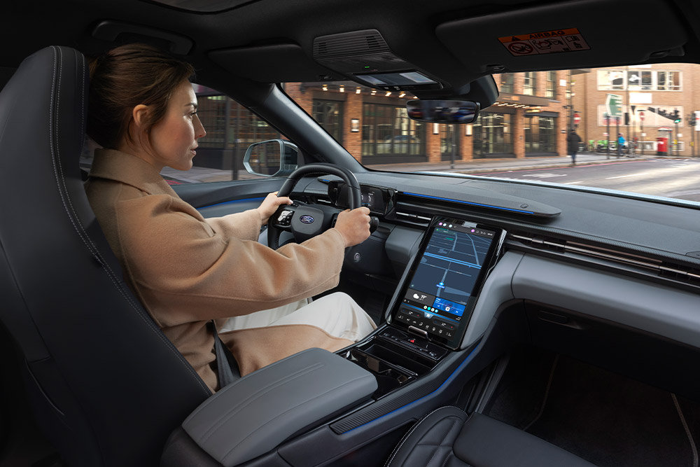  A person driving a Ford Capri, with the large central touchscreen displaying navigation.