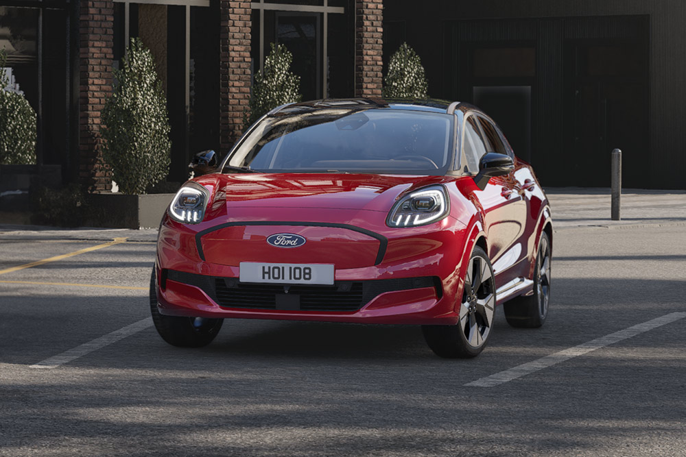 A red Ford Puma Gen-E electric vehicle driving along a city road.