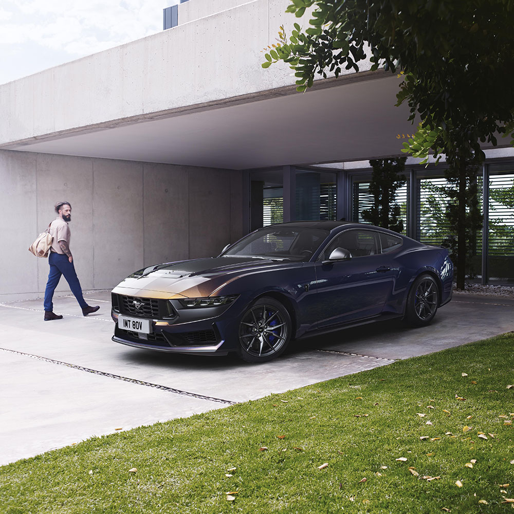 Navy blue Ford Mustang parked on a driveway as a person walks by checking it out.