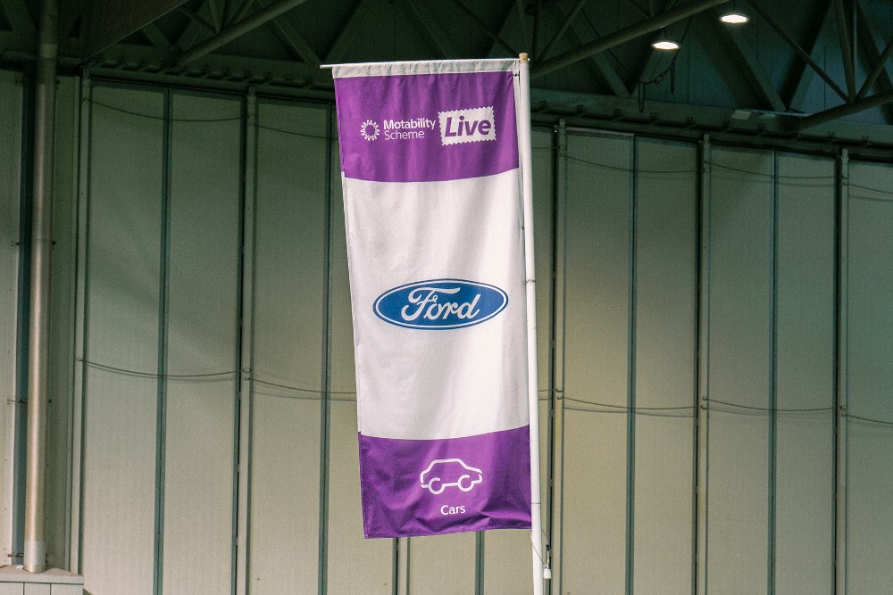 A Ford flag featuring the Ford logo, “Motability Scheme Live" text, and a car icon.